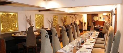 Una larga mesa de comedor con sillas, una araña y paneles decorativos en la pared.