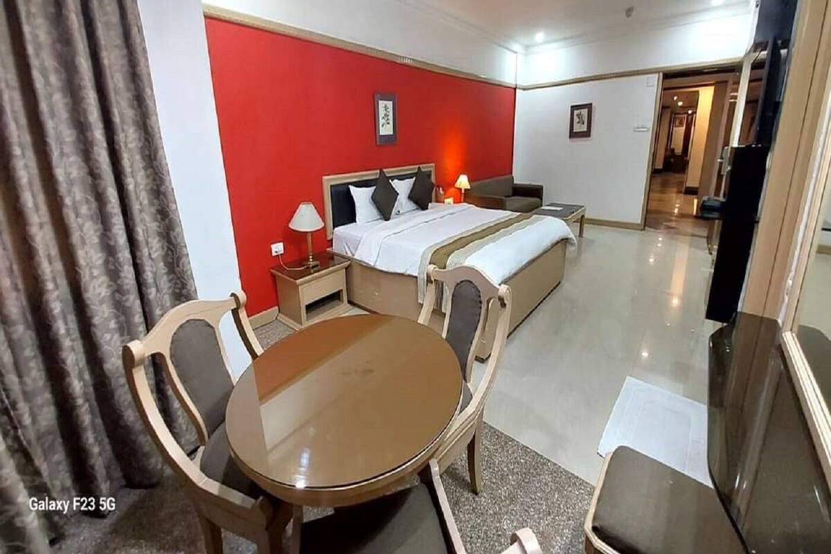 A hotel room with a bed, bedside table, lamp, and a dining area with a table and chairs.