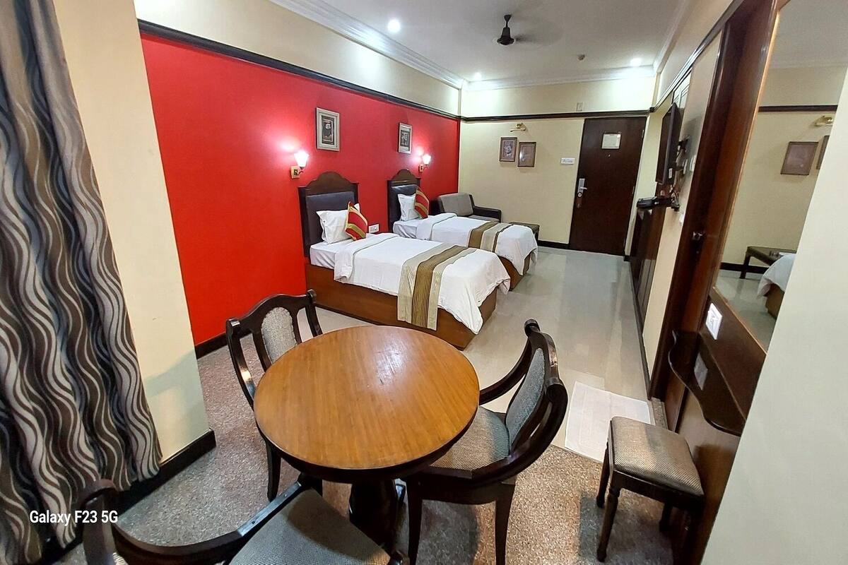 A hotel room with a red accent wall, a round wooden table, four beds, and a ceiling fan.