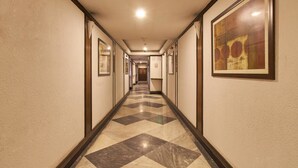A hotel hallway with a checkered floor, framed pictures on the walls, and a ceiling light. - Lytton Hotel (Kolkata)