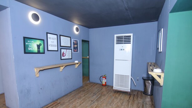 A room with a wooden floor, a white air conditioning unit, a wooden shelf, a fire extinguisher, and framed pictures on the wall. - Lytton Hotel (Kolkata)