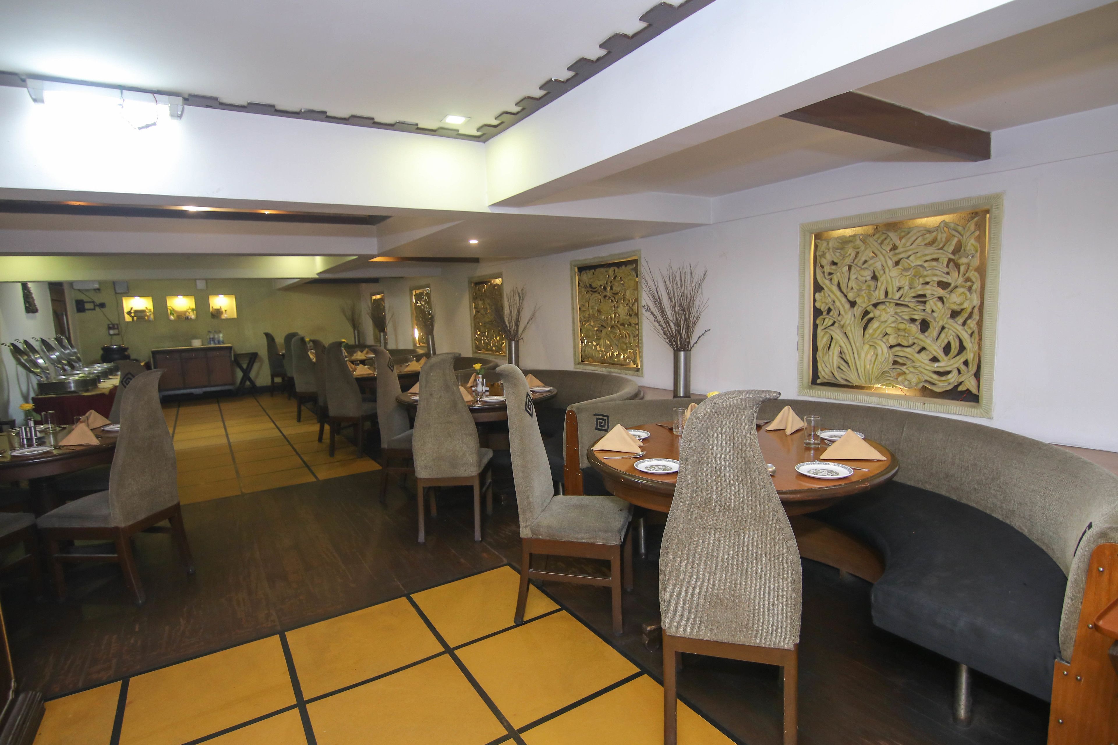A restaurant with multiple dining tables and chairs, a yellow patterned floor, and decorative wall art.