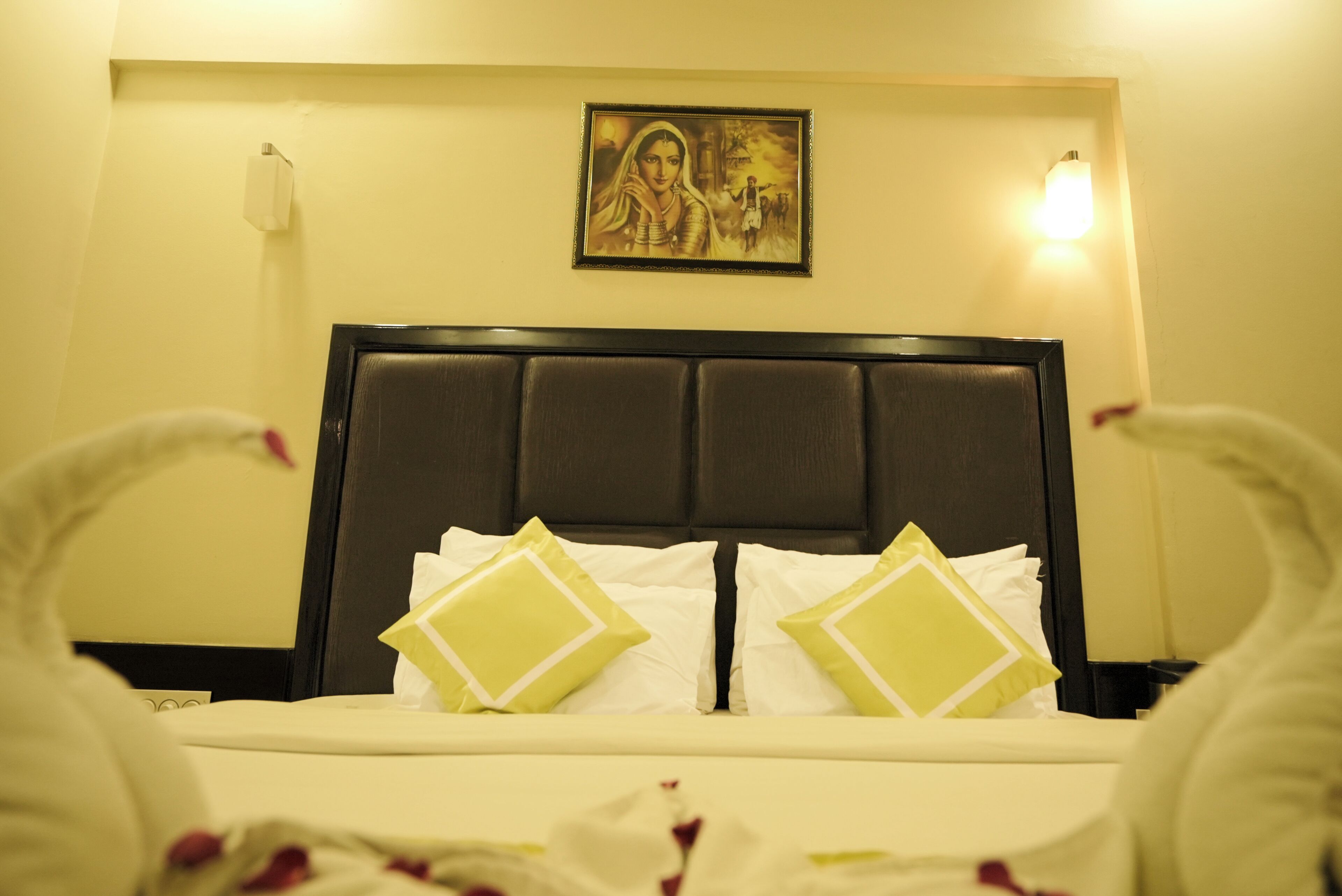 Una habitación de hotel con cama, almohadas, cabecero, un cuadro en la pared y una mesita de noche.