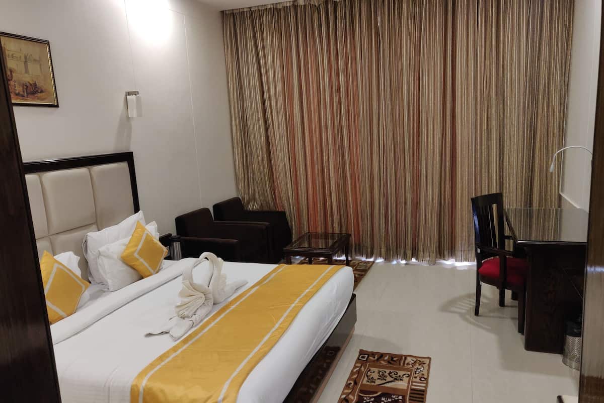 A hotel room with a neatly made bed, a desk, a chair, and a large window with curtains.