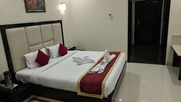 Habitación de hotel con cama, almohadas, toalla, un cuadro, mesita de noche, cafetera y puerta.