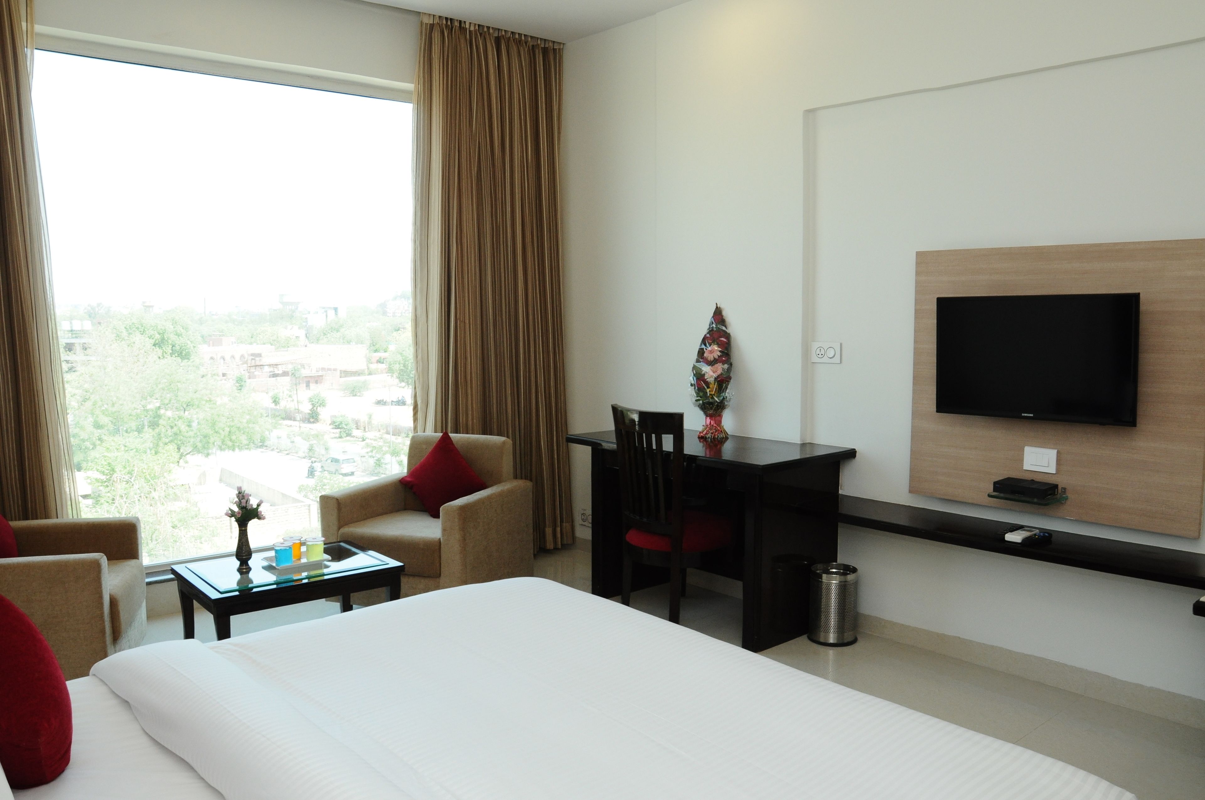 A hotel room with a bed, a desk, a chair, a TV mounted on the wall, and a window with curtains.