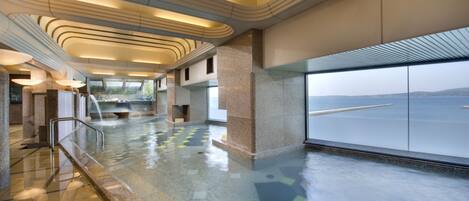 Un amplio espacio interior con una gran fuente de agua, vistas al mar a través de un ventanal y un diseño arquitectónico moderno con líneas curvas y suelo pulido.