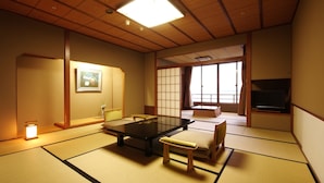 A traditional Japanese room with tatami flooring, a low table, a cushion, a television, and a sliding door. - Kagaya (Nanao)