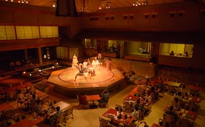 A large indoor space with a central stage surrounded by tables and chairs, suggesting a dining or event venue. - Aenokaze (Nanao)