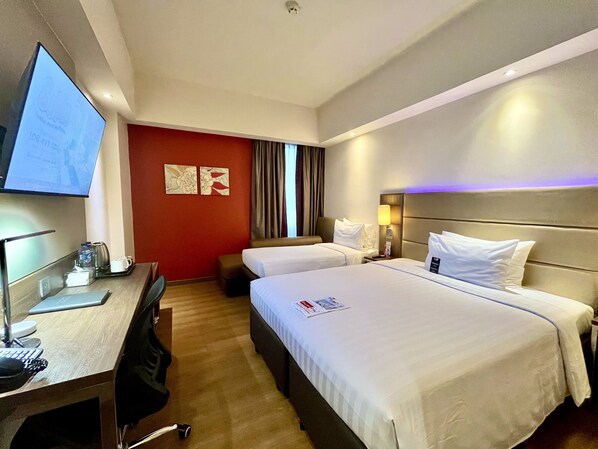 Camera d'albergo con due letti, una scrivania con computer, televisione e macchina del caffè.