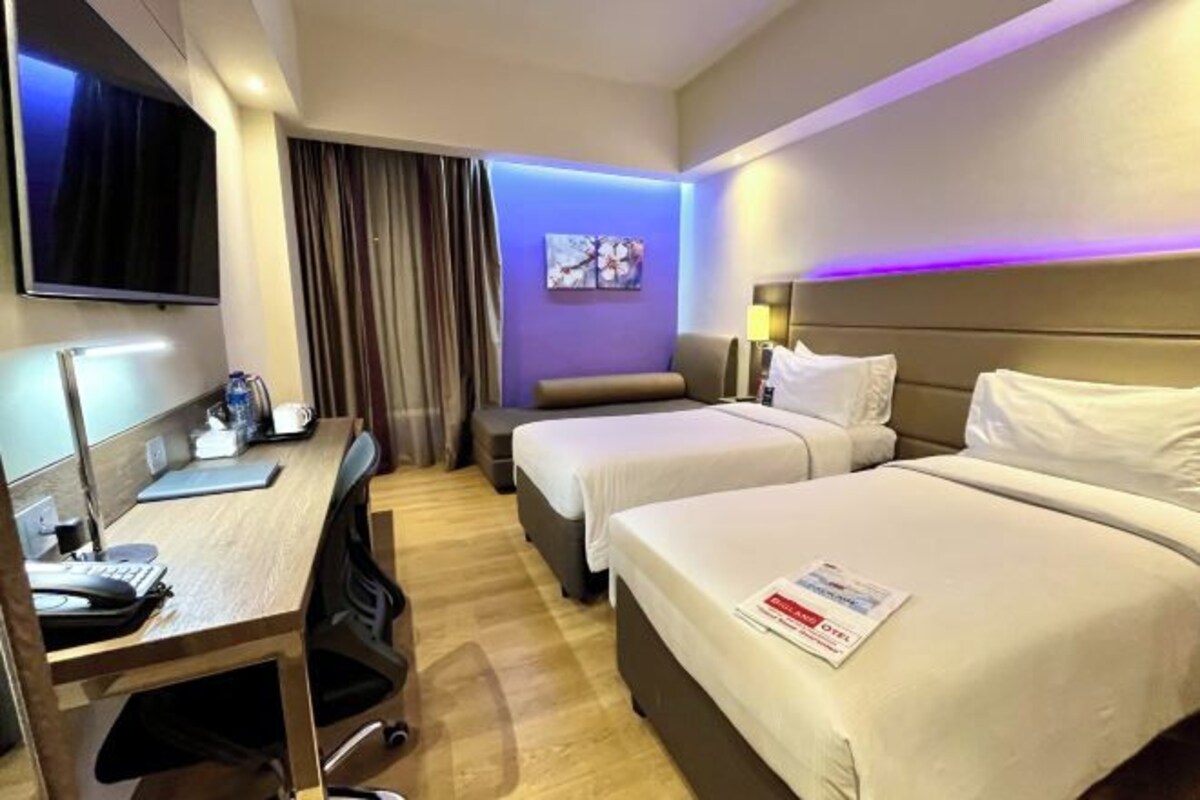 A hotel room with two beds, a desk with a computer, a flat-screen TV, and a painting on the wall.