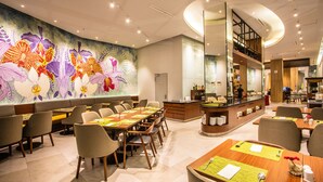 Un restaurante moderno con una larga mesa común, asientos individuales y un mural floral llamativo en la pared.