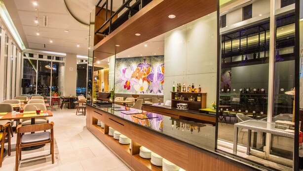 Un área de bar moderna con mostrador de vidrio, asientos y un mural decorativo.