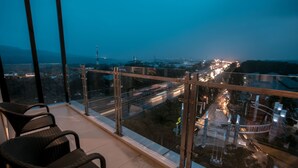 Balcón con barandilla de vidrio que da a una vista panorámica de la ciudad al anochecer.