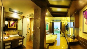 Quarto de hotel com uma cama grande, banheiro com pia e espelho, e vista para o exterior.