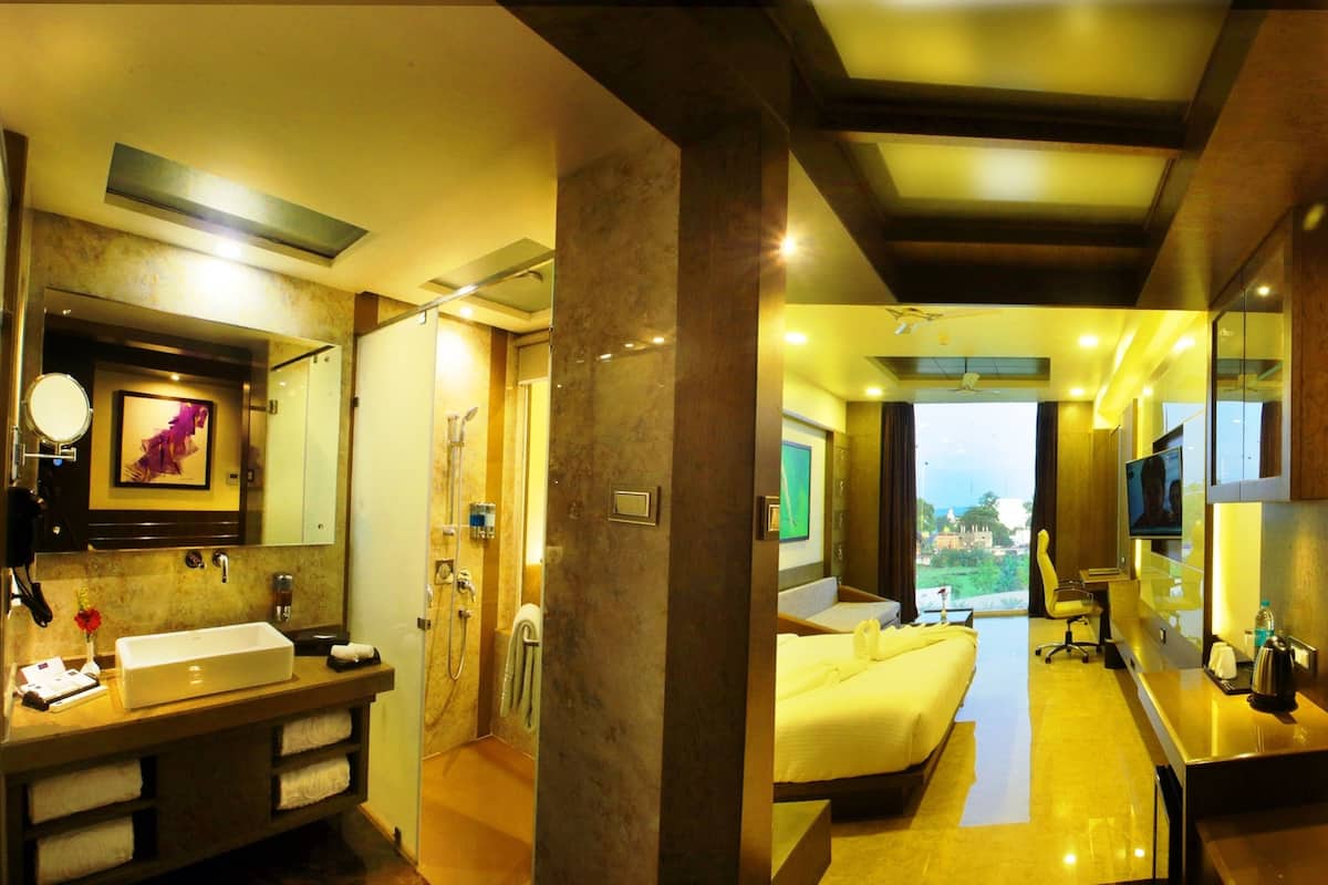Ein Hotelzimmer mit einem großen Bett, einem Badezimmer mit Waschbecken und Spiegel sowie Blick ins Freie.