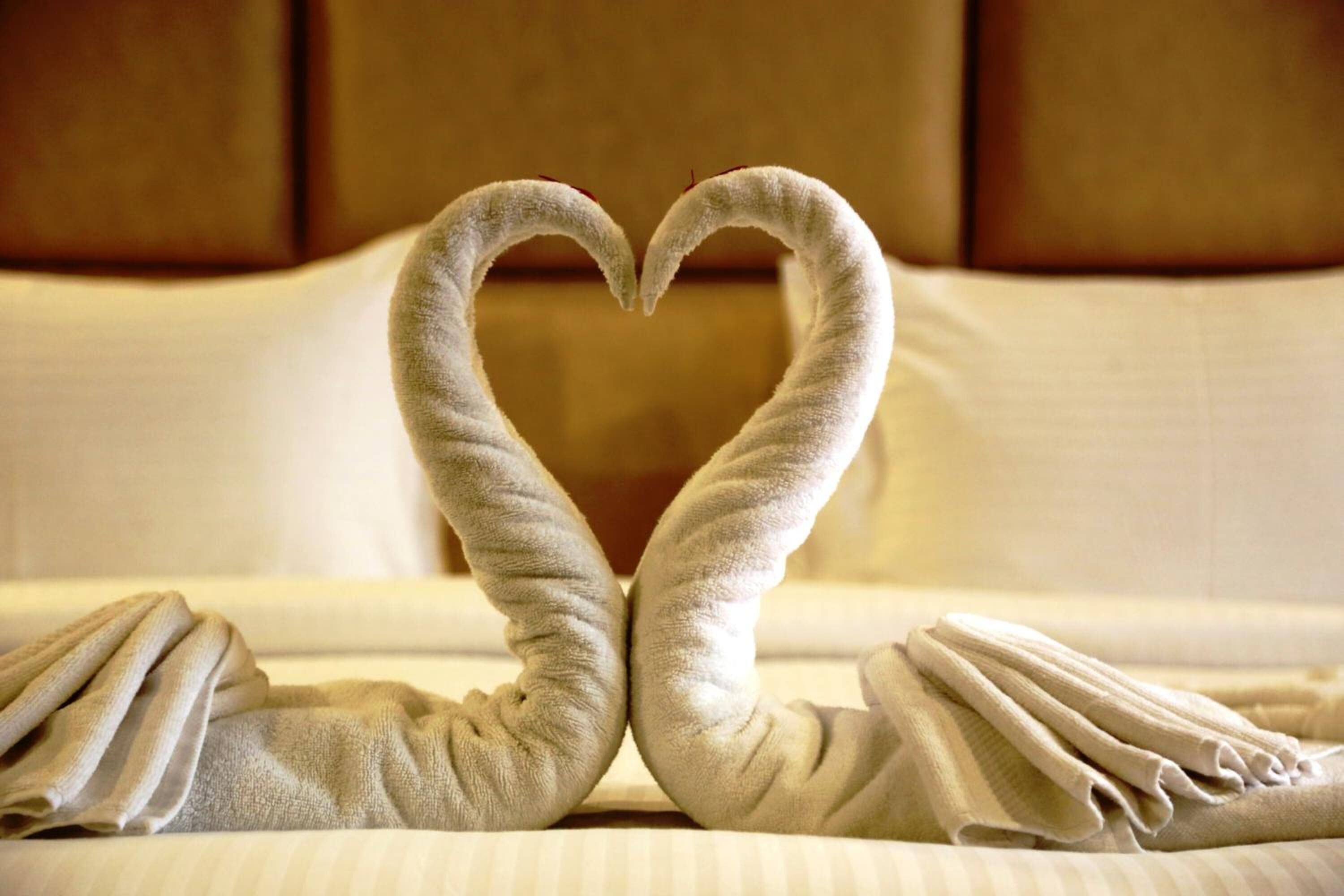 A bed with towels arranged in a heart shape.