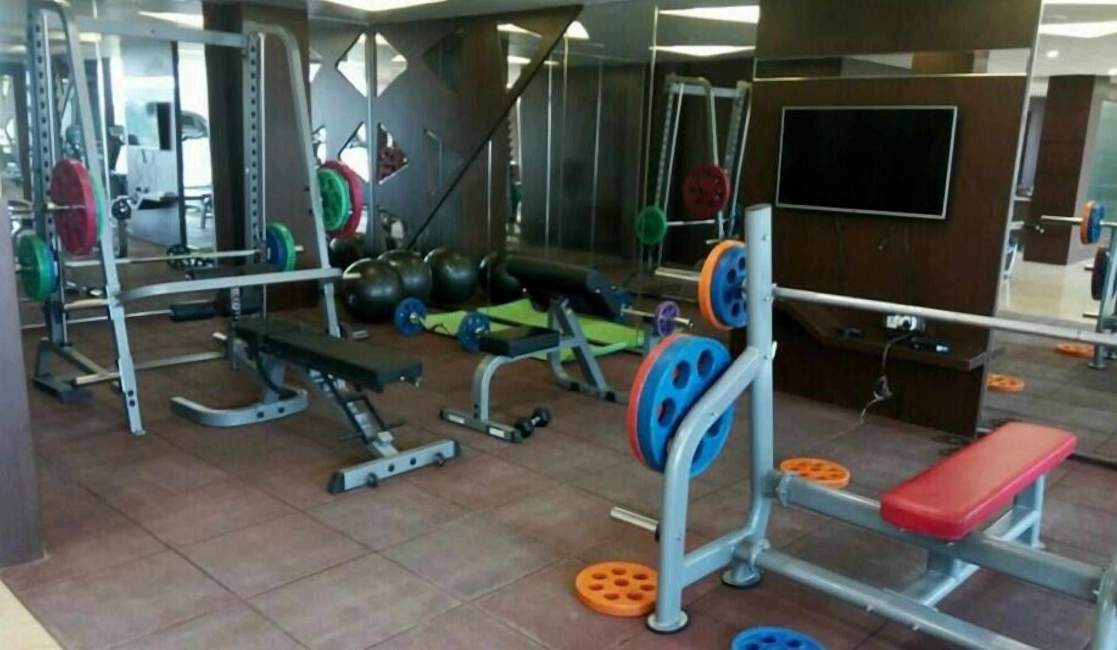 Un gimnasio con equipo de levantamiento de pesas, bancos y un espejo.