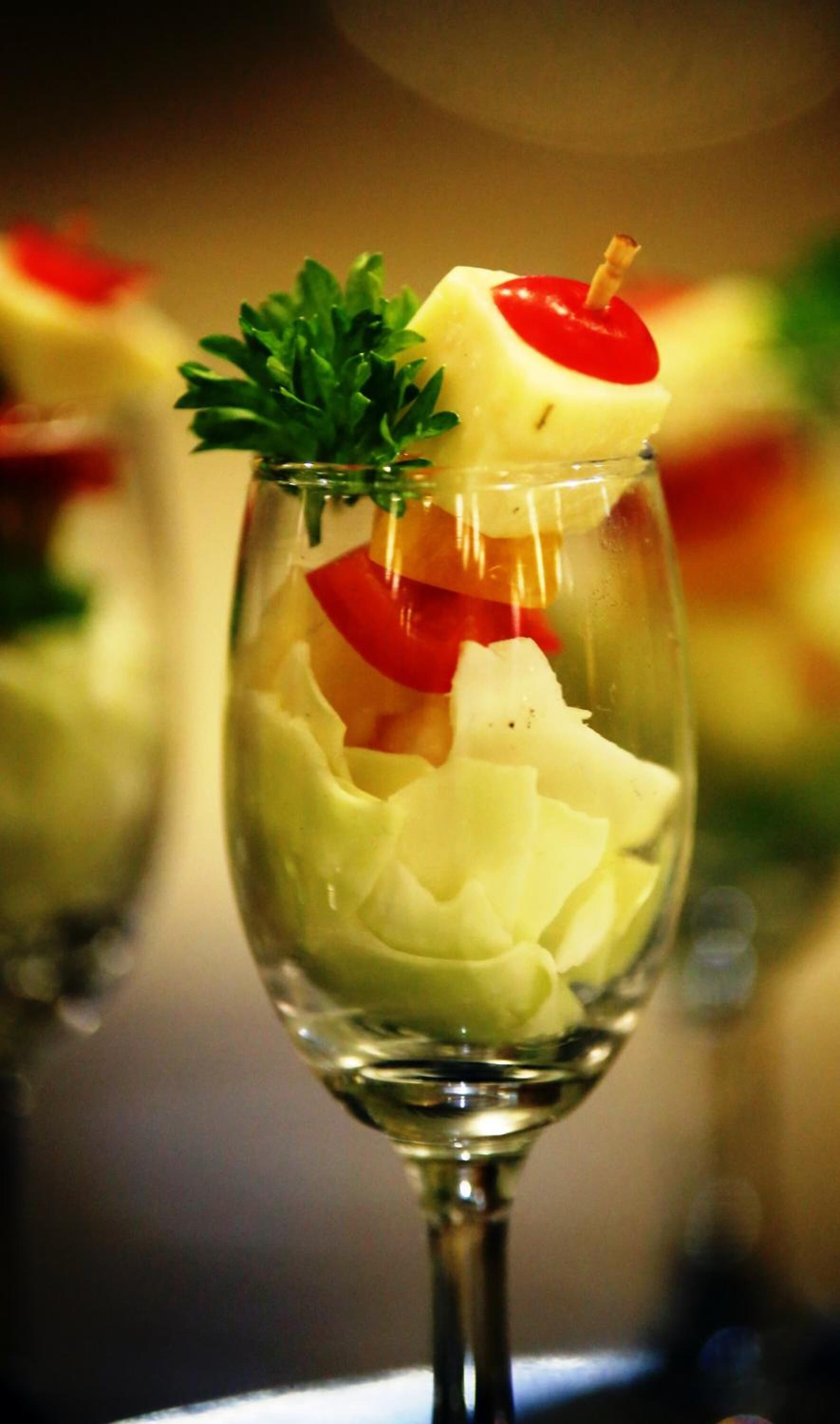 Un vaso con una ensalada en capas, que incluye lechuga, tomates y una cereza roja en la parte superior.