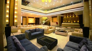 Um hall amplo com várias áreas de estar, uma escadaria central e um lustre moderno.