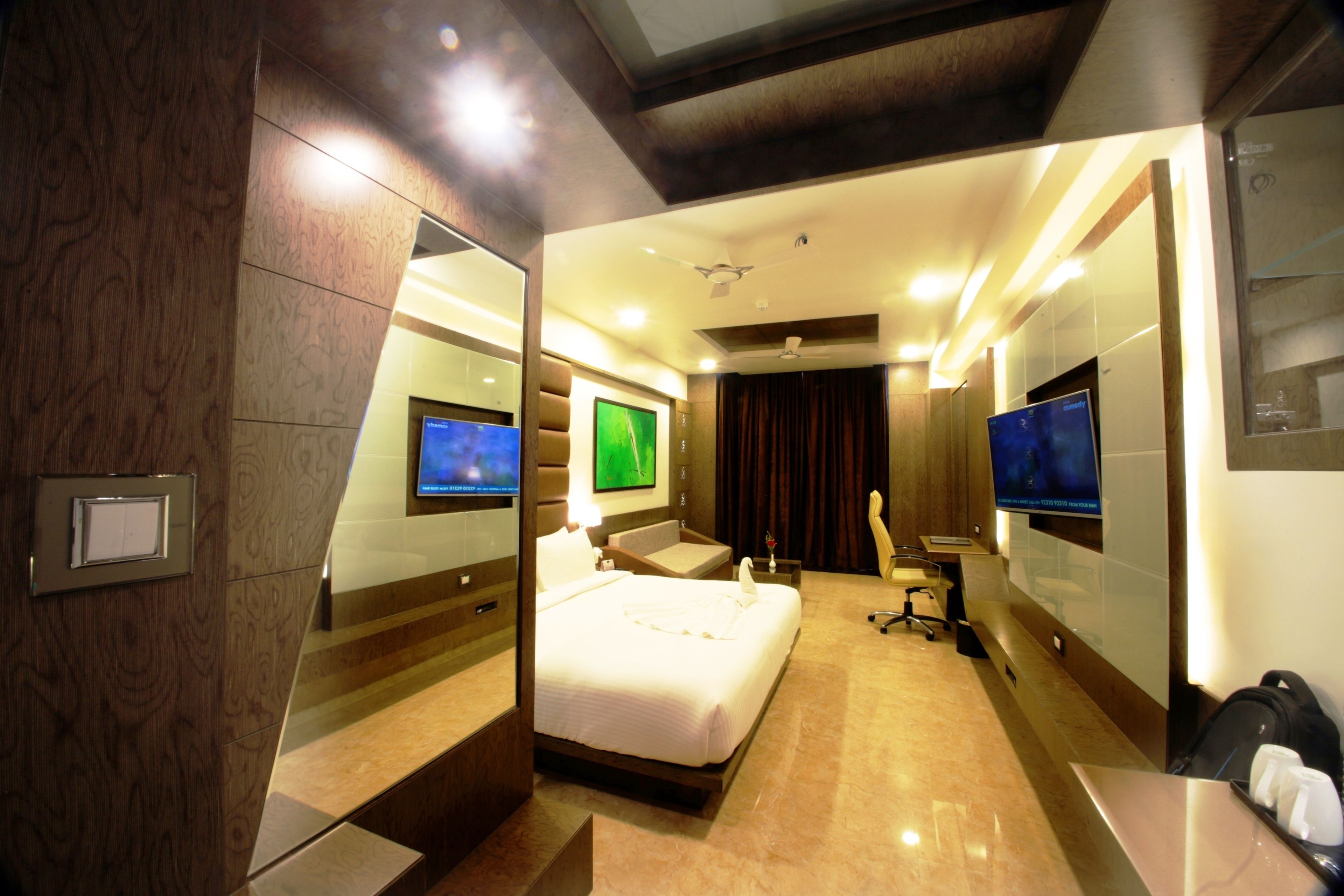 A modern hotel room with a large bed, two TVs, a desk, and a chair.