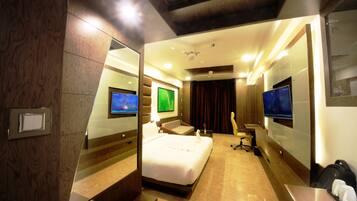 A modern hotel room with a large bed, two TVs, a desk, and a chair.