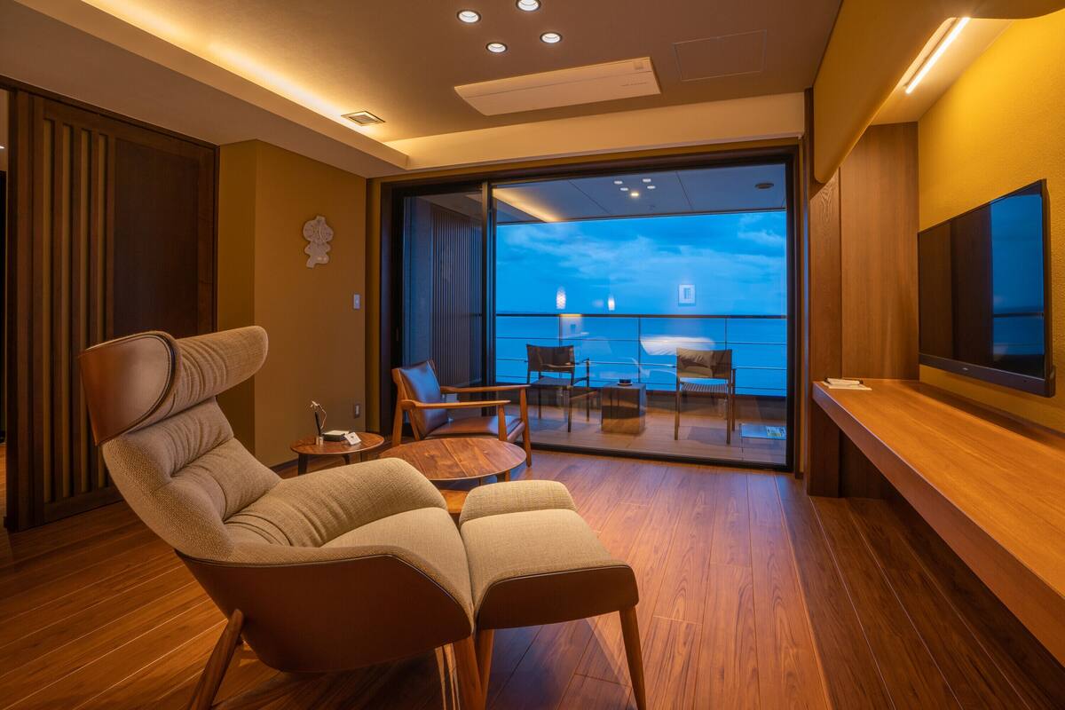A modern hotel room with a large window, a comfortable seating area, and a flat-screen TV.
