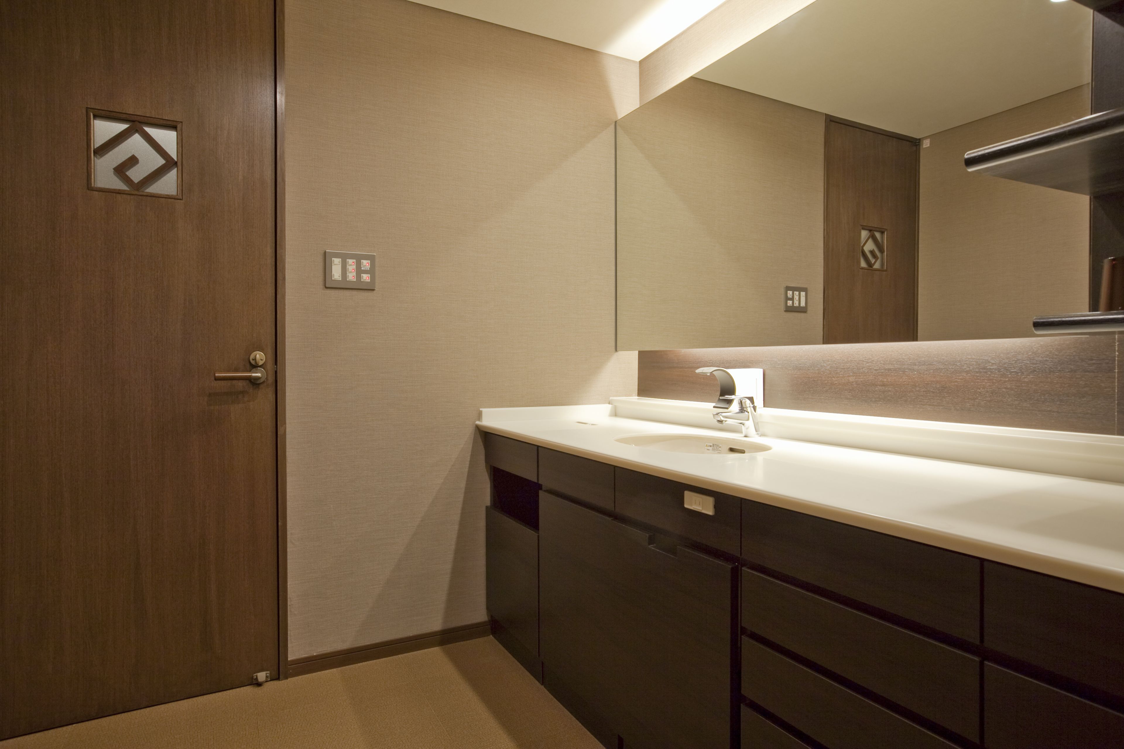 A modern bathroom with a wooden door, a white sink, and a large mirror.