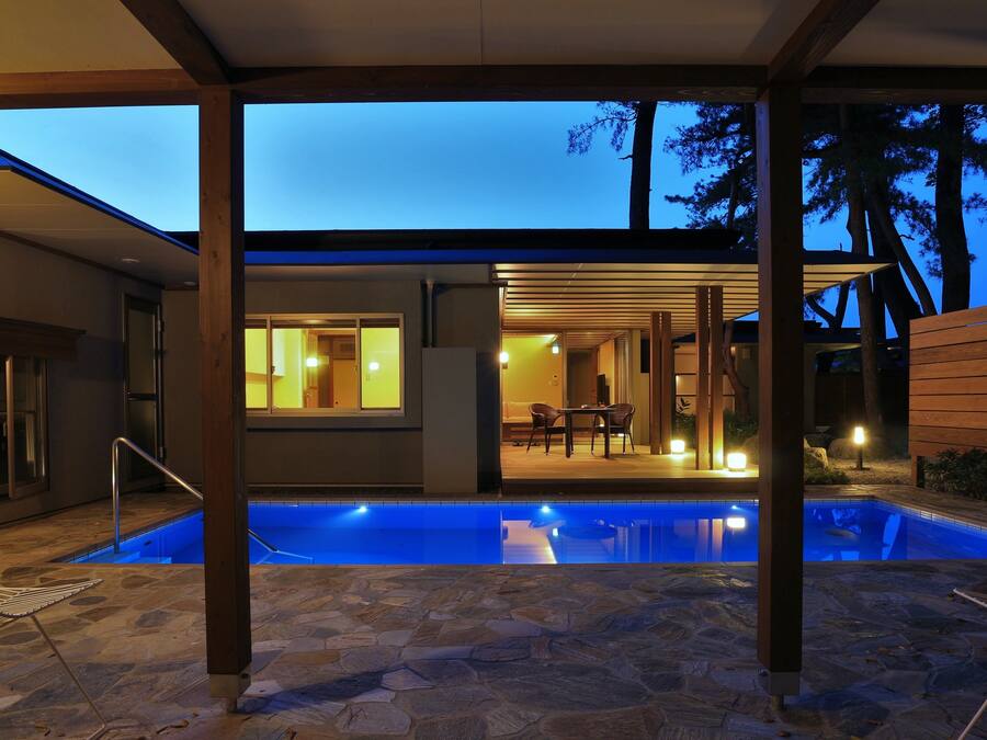 A modern house with a swimming pool, stone flooring, and a covered patio area with a table and chairs.