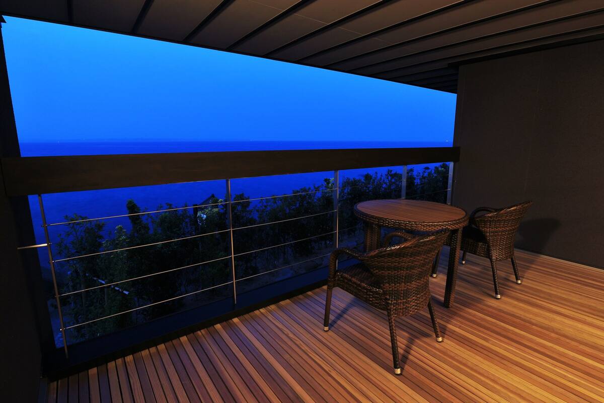 A balcony with a view of the sea, wooden flooring, and wicker chairs.