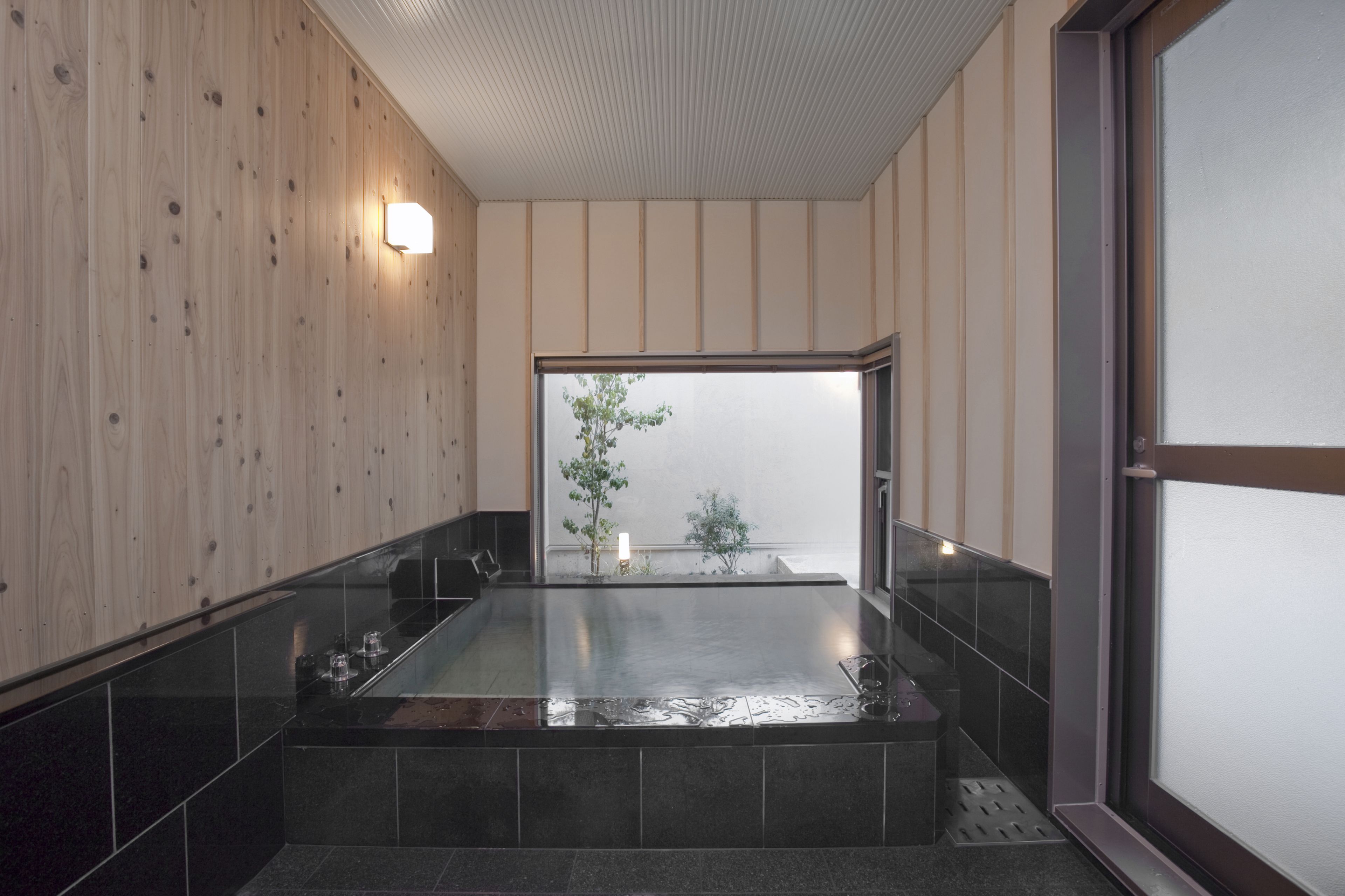 Un baño moderno con una bañera grande, paneles de madera y una ventana pequeña con vistas a la vegetación.