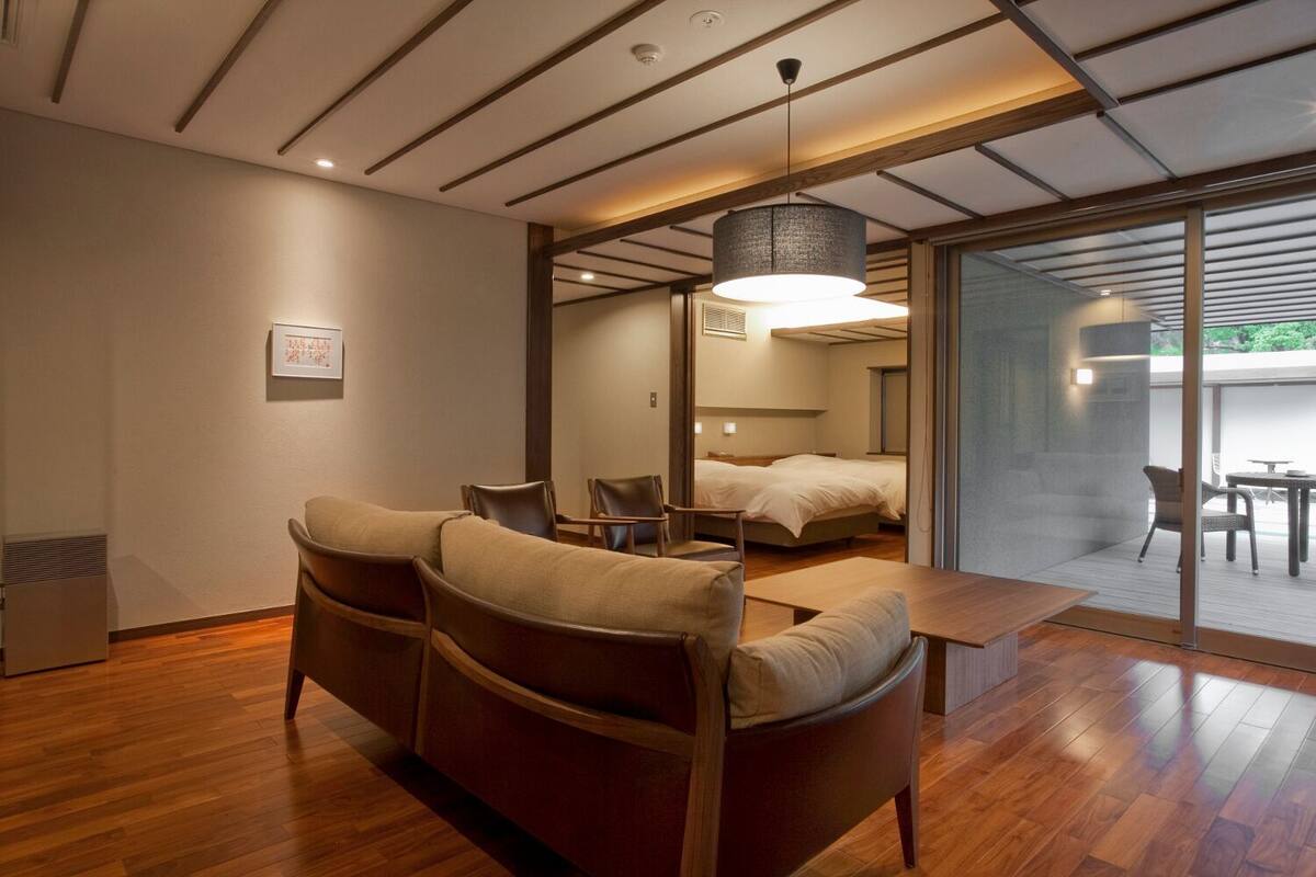 A modern hotel room with a wooden floor, a sofa, a bed, and a dining area.
