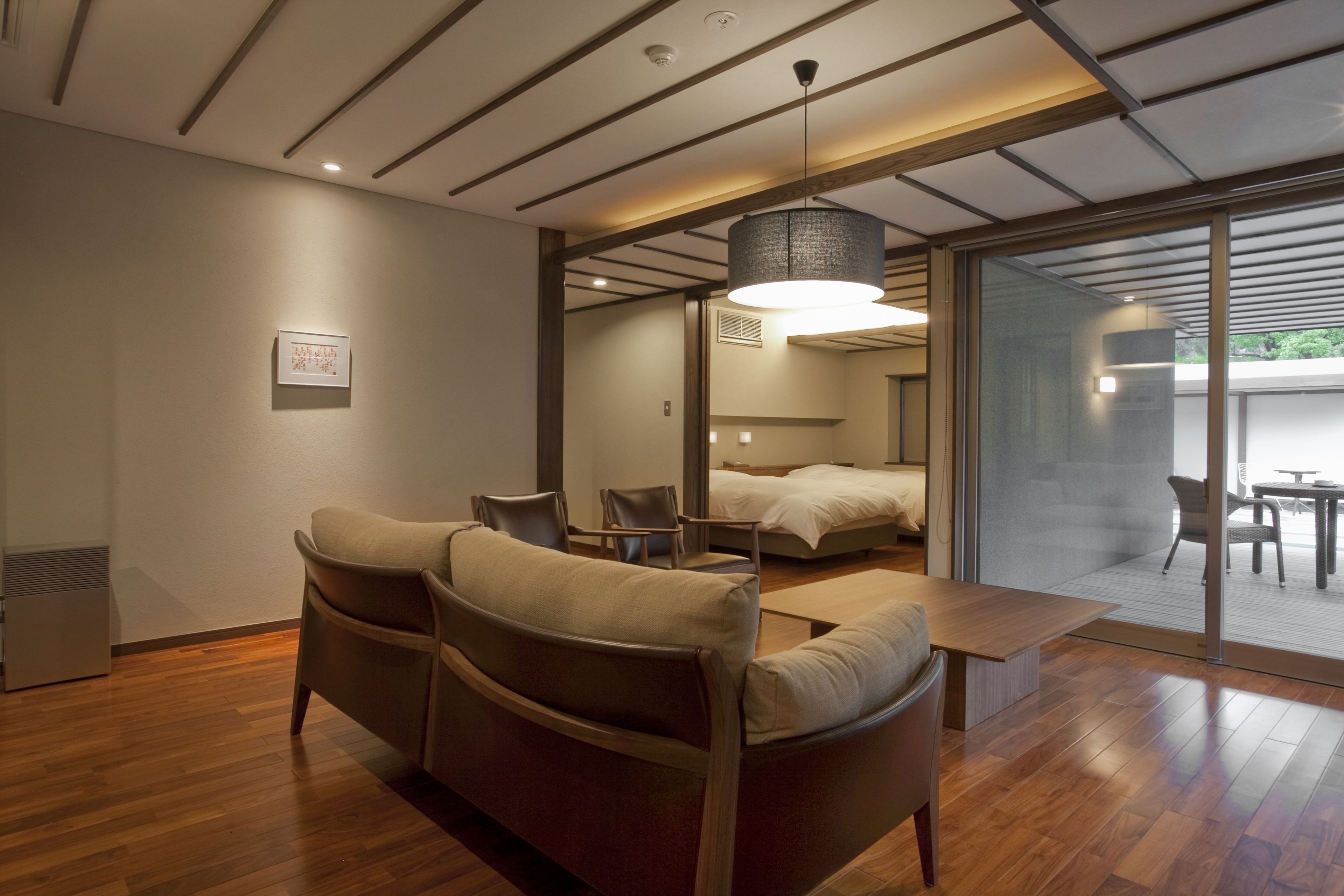 A modern hotel room with a wooden floor, a sofa, a bed, and a dining area.