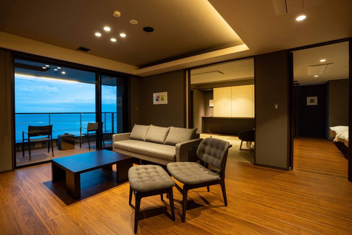 A modern living room with a sofa, two armchairs, a coffee table, and a view of the ocean.