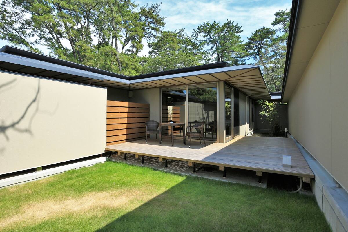 A modern outdoor patio with a wooden deck, glass doors, and a seating area with chairs and a table.