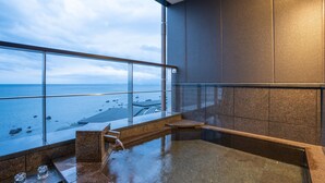 A modern spa area with a large bathtub, a glass railing, and a view of the sea. - Amane Resort Gahama (Beppu)
