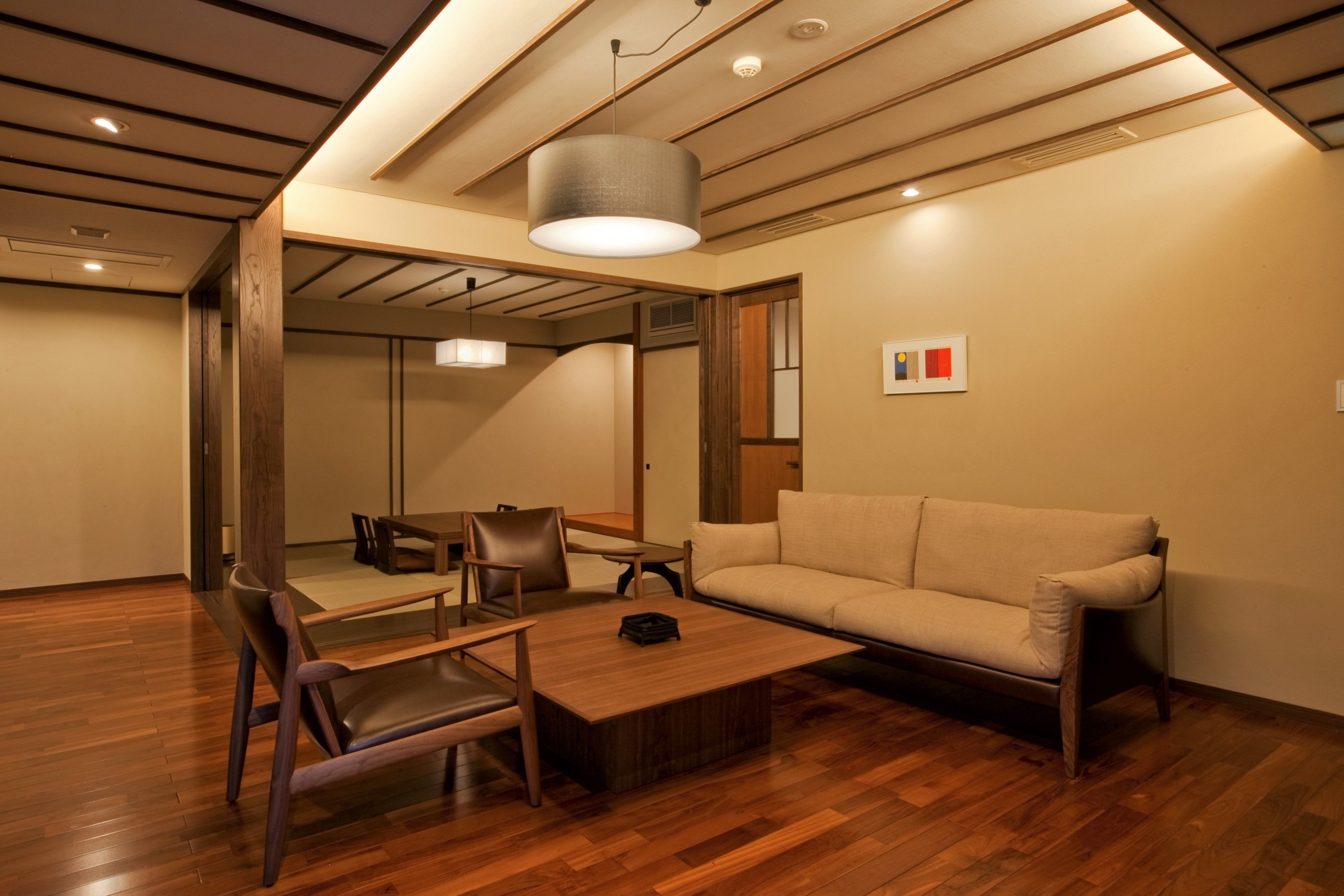 Una sala de estar moderna con piso de madera, un sofá color beige, una mesita de centro y un comedor con sillas y una mesa.