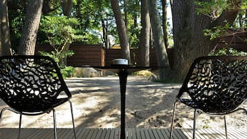 A wooden deck with two metal chairs and a table, surrounded by trees.