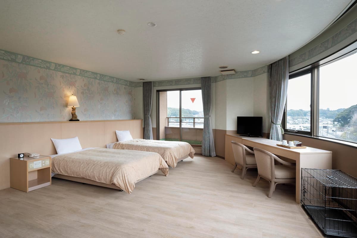 Ett hotellrum med två sängar, ett skrivbord, en TV och ett fönster med utsikt.
