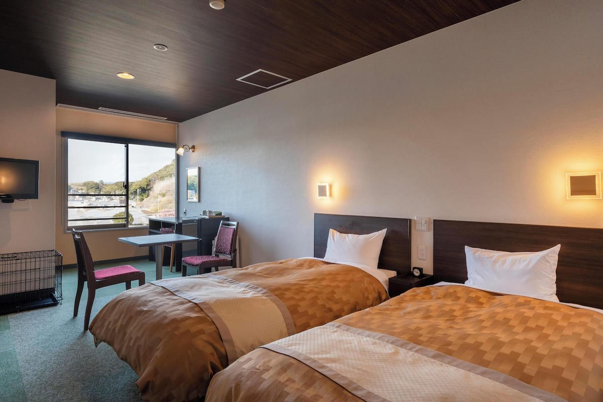 Ett hotellrum med två sängar, ett skrivbord, en stol och ett stort fönster.