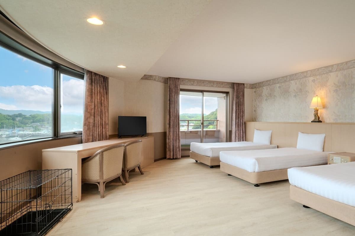 Quarto de hotel com escrivaninha, duas camas, televisão e vista para o exterior.