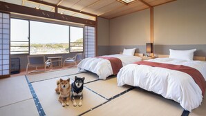 Een hotelkamer met twee bedden, een groot raam met uitzicht, tatami matten en twee honden.