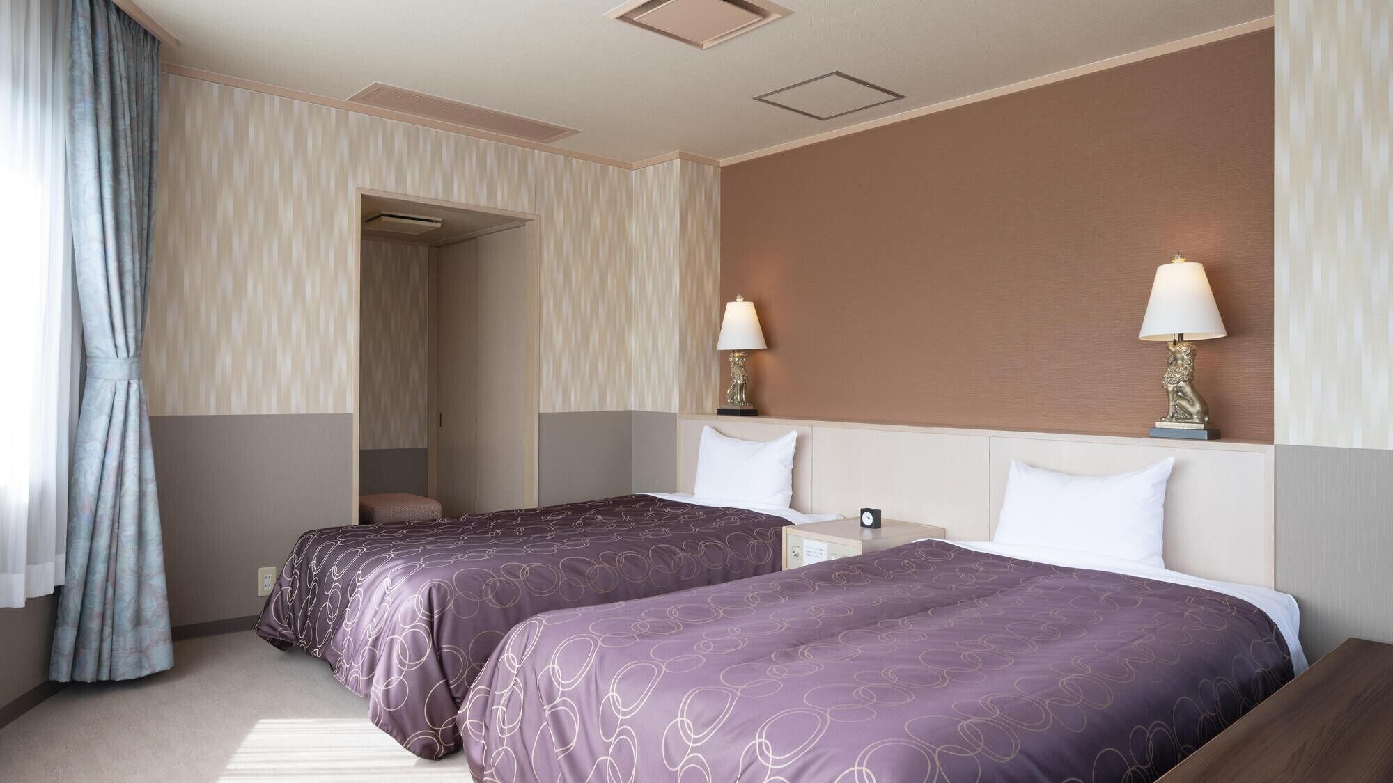 A hotel room with two beds, a nightstand, a lamp, and a wardrobe.