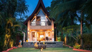 A two-story house with a triangular roof, a balcony, and a well-lit entrance. - Villa Manipura (Ko Chang)