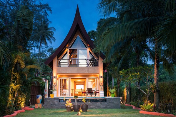Una casa de dos pisos con techo triangular, balcón y una entrada bien iluminada.