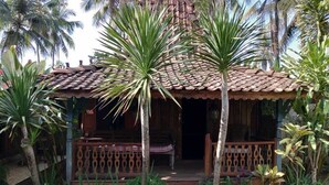 Ein rustikales Haus mit Ziegeldach, einer Holzveranda und einem Garten mit Palmen.