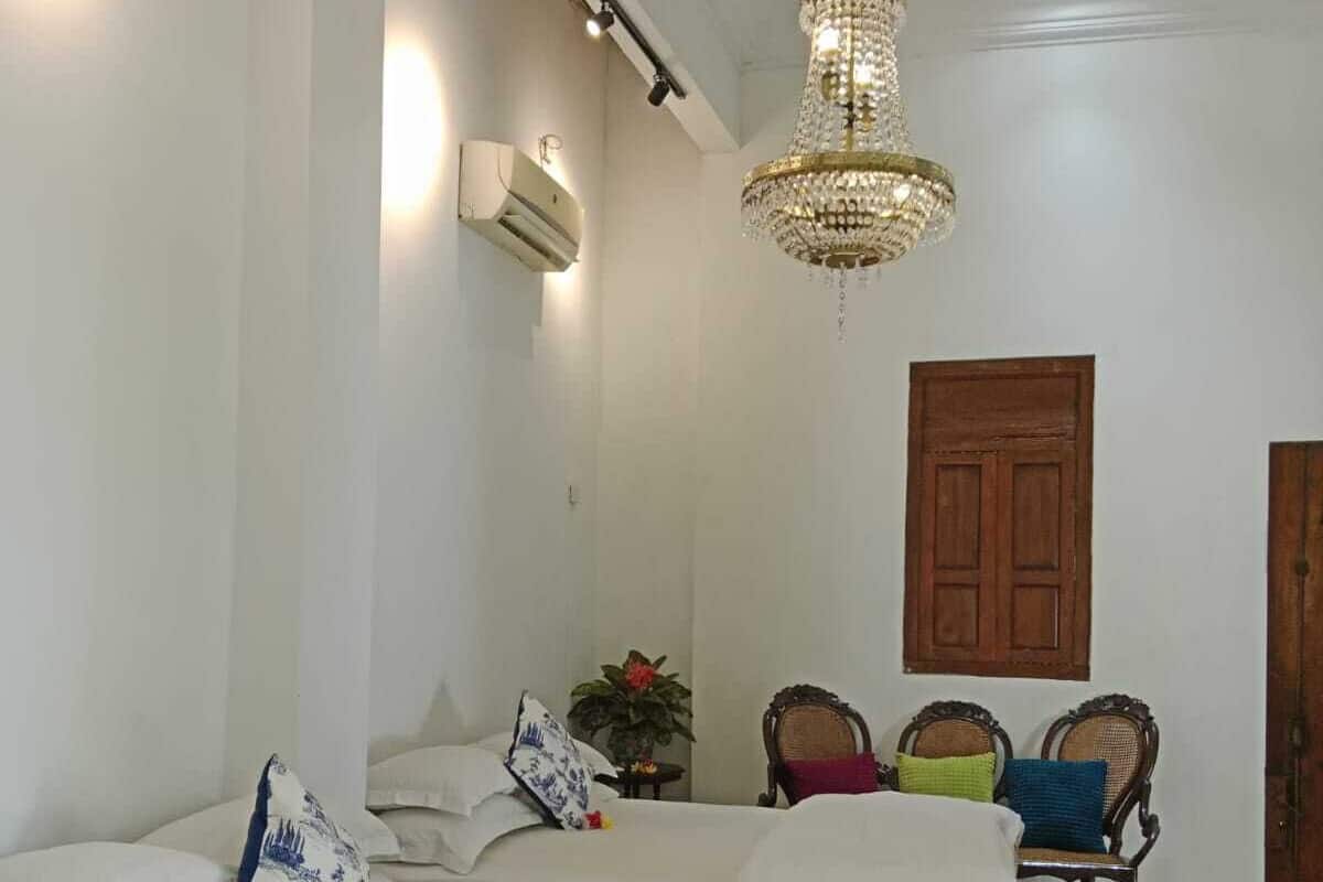 Quarto com cama, lustre, porta de madeira e piso estampado.