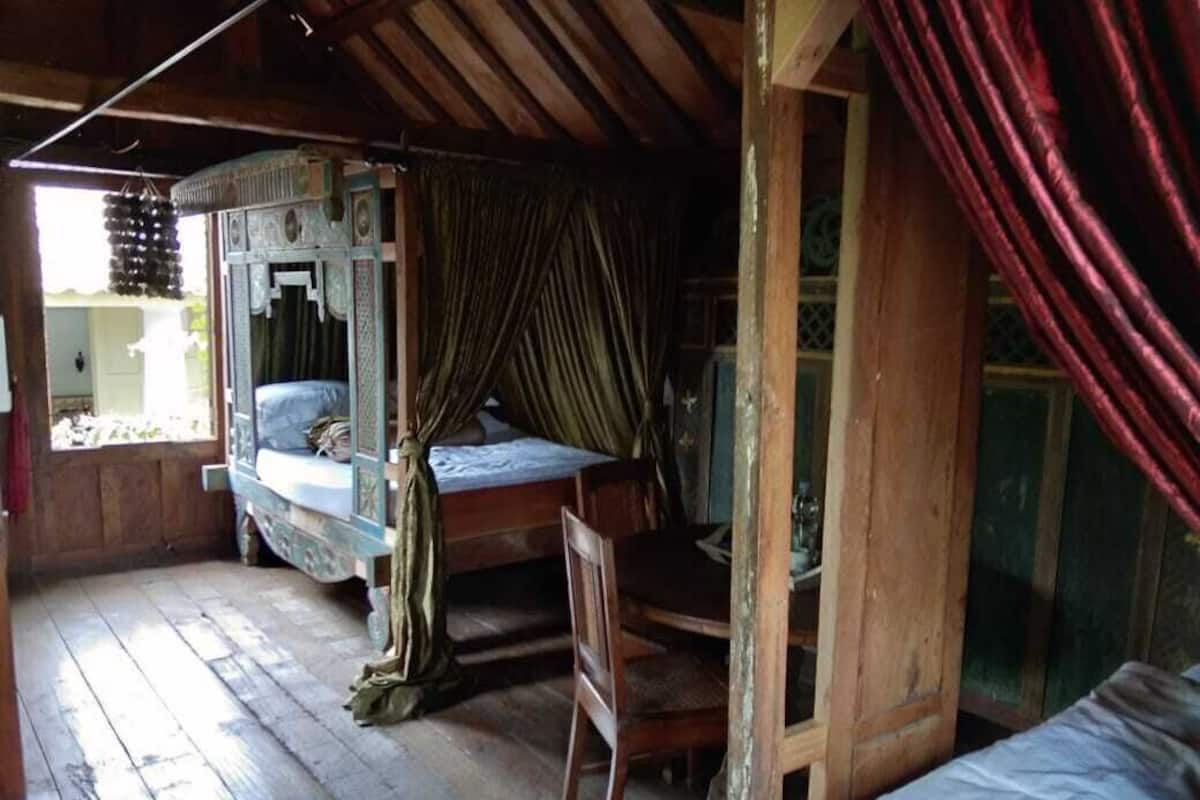 Um quarto rústico com cama de madeira, uma cadeira e uma janela com cortinas.