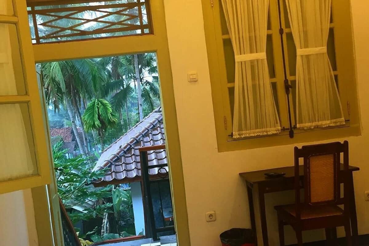 Quarto com cama, cadeira, mesa pequena, televisão fixada na parede e janela com cortinas.