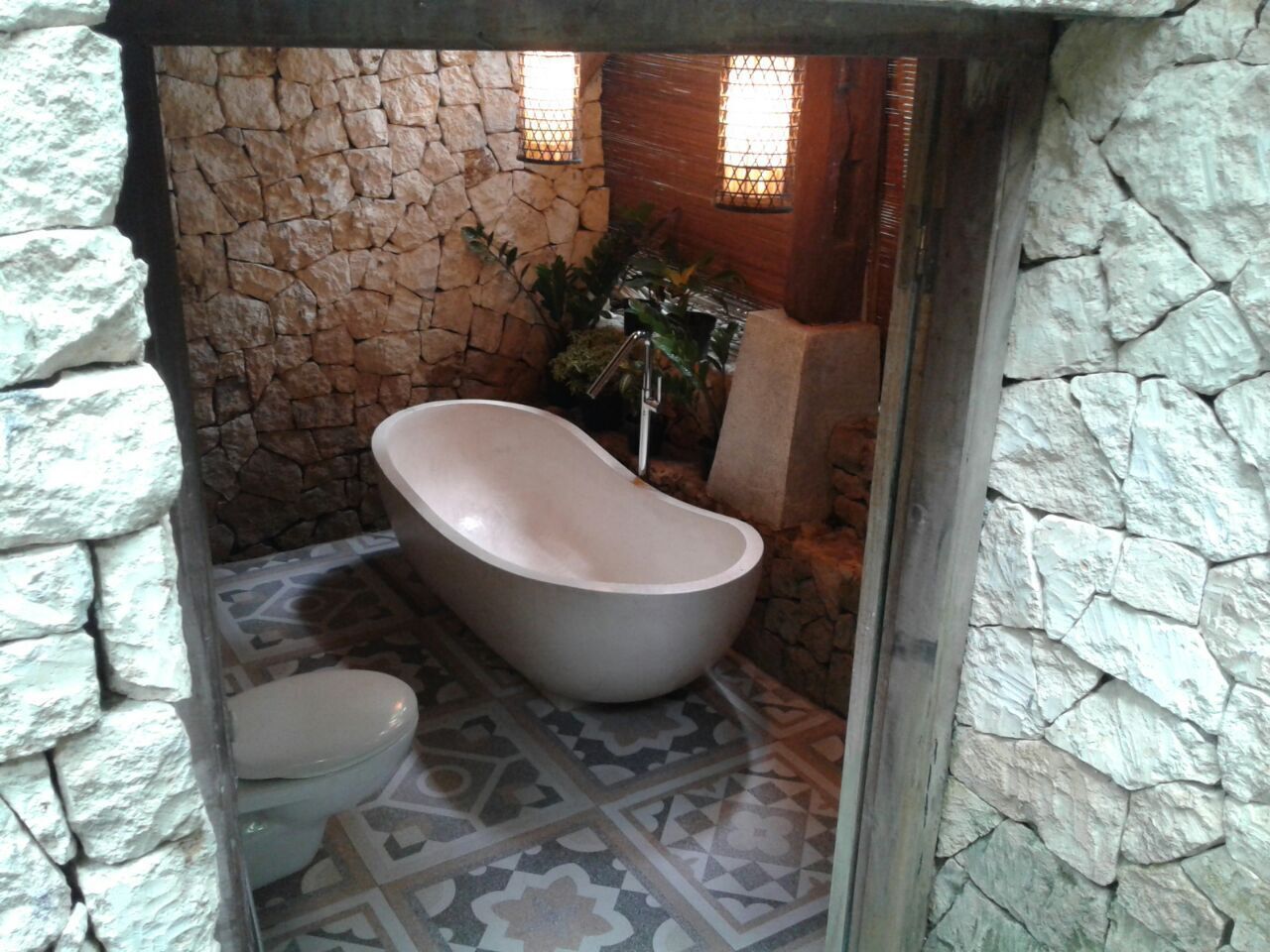 A bathroom with a freestanding bathtub, a toilet, and patterned floor tiles.